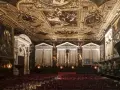 Sala capitolare Scuola Grande di San Rocco: soffitto dorato affrescato, pareti con dipinti e statue, sedie rosse disposte per un evento.