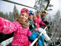 Rodzina na wyciągu narciarskim, robiąca selfie. Dziewczynka z przodu uśmiecha się szeroko. To ich wymarzone wczasy pod gruszą, ale zimowe!