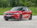 Czerwony Opel Corsa E na tle zieleni. Zbliżenie na przód auta, gdzie widoczne są światła LED i tablica rejestracyjna. Poznaj opel corsa e wymiary.