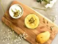 Aksamitny mango lassi w szklance, posypany pistacjami. Obok miseczka jogurtu, dojrzałe mango i kardamon.