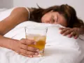Kobieta w łóżku z drinkiem, nieświadoma. Objawy po zażyciu pigulka gwaltu mogą być różne.
