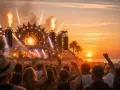 Tłum ludzi na plaży, płomienie buchające ze sceny, zachód słońca i muzyka na Sunrise Festival 2026.