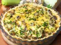 Pyszny quiche z pieczarkami, posypany świeżą natką pietruszki, w szklanej formie.