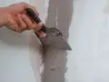 Mano che usa una spatola per stuccare un muro, creando una superficie liscia e uniforme per la pittura.