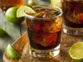 Orzeźwiający Cuba Libre, czyli rum z colą i limonką, z kostkami lodu i świeżymi ćwiartkami cytrusów na drewnianym blacie.