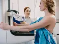 Kobieta przygotowuje się do mammografii, podczas gdy radiolog uśmiecha się wspierająco.