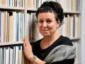 Olga Tokarczuk, w swoim wieku, otoczona książkami, z dłonią na grzbietach.