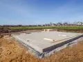 Betonowe ławy fundamentowe gotowe na nowy dom. W tle widać domy i zielone pola.