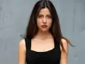 Ritratto di una giovane donna con lunghi capelli castani, indossa un abito nero. Il suo sguardo è intenso, come se stesse aspettando qualcuno, forse celeste dalla porta.