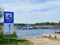 Znaki informują o 133 km do Gowidlina i o jeziorze Gowidlińskim. Widok na pomost z żaglówkami i kajakiem.