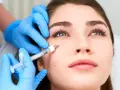 Manos enguantadas aplican inyección para tratar arrugas debajo de los ojos.