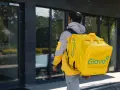 Kurier Glovo pieszo idzie z żółtą torbą na plecach.