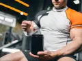 Mężczyzna w sportowej koszulce przygotowuje porcję kreatynowy.