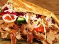 Kebab z mięsem, warzywami i sosem w bułce na drewnianym tle.