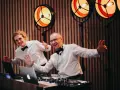 Dwóch DJ-ów w białych koszulach i czarnych muszkach, z uśmiechem na twarzy, przygotowuje się do imprezy. Zastanawiasz się, ile kosztuje DJ na wesele?