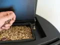 Mano cargando pellets en una estufa de pellets. Preparando la instalación de la estufa de pellets para un invierno cálido.
