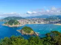 Widok na zatokę La Concha w Donostia San Sebastian, z zielonymi wzgórzami, miastem i licznymi łodziami na turkusowej wodzie.