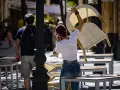 Una mujer con el pelo teñido de rojo, en plena faena de hostelería, apila sillas mientras habla por teléfono.