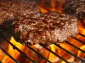 Soczyste kotlety wołowe smażące się na grillu z płomieniami.