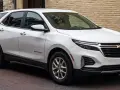 Biały Chevrolet Equinox, wszechstronny chevrolet suv, zaparkowany na brukowanej ulicy przed ceglanym budynkiem.