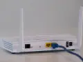 Biały modem z dwiema antenkami, podłączony niebieskim kablem Ethernet. To urządzenie, które pozwala na połączenie z internetem.