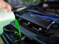 A hand pours bright green coolant into a car's radiator. This prevents the engine from overheating, unlike if coolant were mixed with oil.