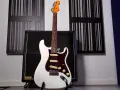 Weiße E-Gitarre mit sechs Saiten steht vor einem Verstärker.