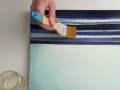 Main d'artiste appliquant une couche de vernis sur une toile aux rayures bleues et blanches. Quel vernis !