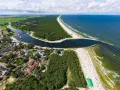 Widok z lotu ptaka na miasteczko nad zatoką, las i plażę. Na falochronie widać czerwoną latarnię morską kikut.