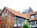 Tradycyjna **konstrukcja muru pruskiego** z ceglanymi wypełnieniami i drewnianymi belkami, obok nowoczesnych budynków.
