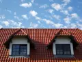 Dachówka ceramiczna w kolorze ceglastym pokrywa dach domu z dwoma lukarnami. Różne rodzaje dachówek tworzą harmonijną całość.