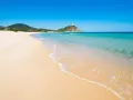 Piękne plaże Cagliari z turkusową wodą i piaszczystym brzegiem. W oddali widać wzgórze z wieżą.