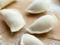 Surowe pierogi na drewnianej desce, przygotowane z ciasta na pierogi bez jajka.