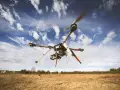 A drone hovers in a blue, cloudy sky over a dry, grassy field, hinting at the need to understand **Montana drone laws** before flying.