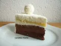 Ein Stück Schoko Kokos Torte mit Kokosraspeln und einer Praline obendrauf.