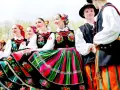 Młodzi ludzie w barwnych strojach ludowych, gotowi do wykonania polskich tańców narodowych.