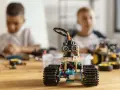 Dzieci budują roboty, ucząc się programowania i inżynierii. W centrum mały robot z czujnikami, w tle chłopcy pracujący nad projektami.