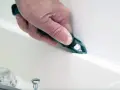 A hand uses a tool to smooth fresh caulk along a bathtub seam, demonstrating how to caulk for a clean finish.