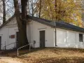 Ohel cadyka Elimelecha w Leżajsku zwiedzanie. Biały budynek z drzwiami i oknem, otoczony drzewami jesienią.