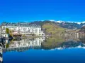 Grand Hotel nad jeziorem w Zell am See, z odbiciem w spokojnej wodzie i ośnieżonymi górami w tle.