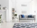 Nowoczesny salon z klimatyzacją w trybie funkcja dry, szara kanapa, kominek, regał i dywan.
