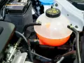 A car's coolant reservoir, showing the orange fluid level. This helps determine how much coolant does a car take.