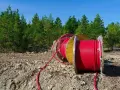Czerwony kabel na drewnianym bębnie, przygotowany do uzbrojenia działki. W tle las i błękitne niebo.