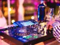 Main d'un dj house connu manipulant la console, lumières vives et ambiance festive.