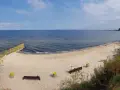 Piękna, piaszczysta plaża dla psów z łagodnym zejściem do morza. W oddali widać falochron i statki.