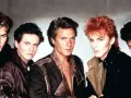 Fünf Männer mit auffälligen Frisuren und 80er-Jahre-Mode, die an ikonische Musikvideos dieser Ära erinnern.