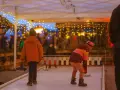 Kinder spielen Eisstockschießen auf einem Weihnachtsmarkt in Berlin. Lichterketten leuchten im Abendlicht.