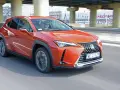 Pomarańczowy Lexus UX 250h jedzie po miejskiej drodze pod wiaduktem.
