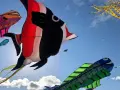 Bunte Drachen in Fischform tanzen am Himmel beim Fehmarn Drachenfest. Ein großer roter und schwarzer Fischdominiert, daneben ein grüner Fisch und ein gelber Tintenfisch.