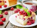 Malinowa chmurka z serem i malinami, udekorowana listkiem mięty. Obok filiżanka herbaty i świeże maliny.